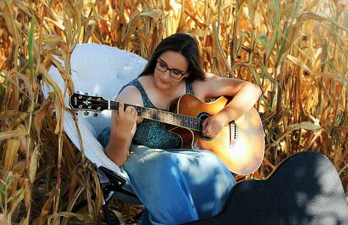 leisure activities woman playing guitar sitting on white chair on corn field musical instrument